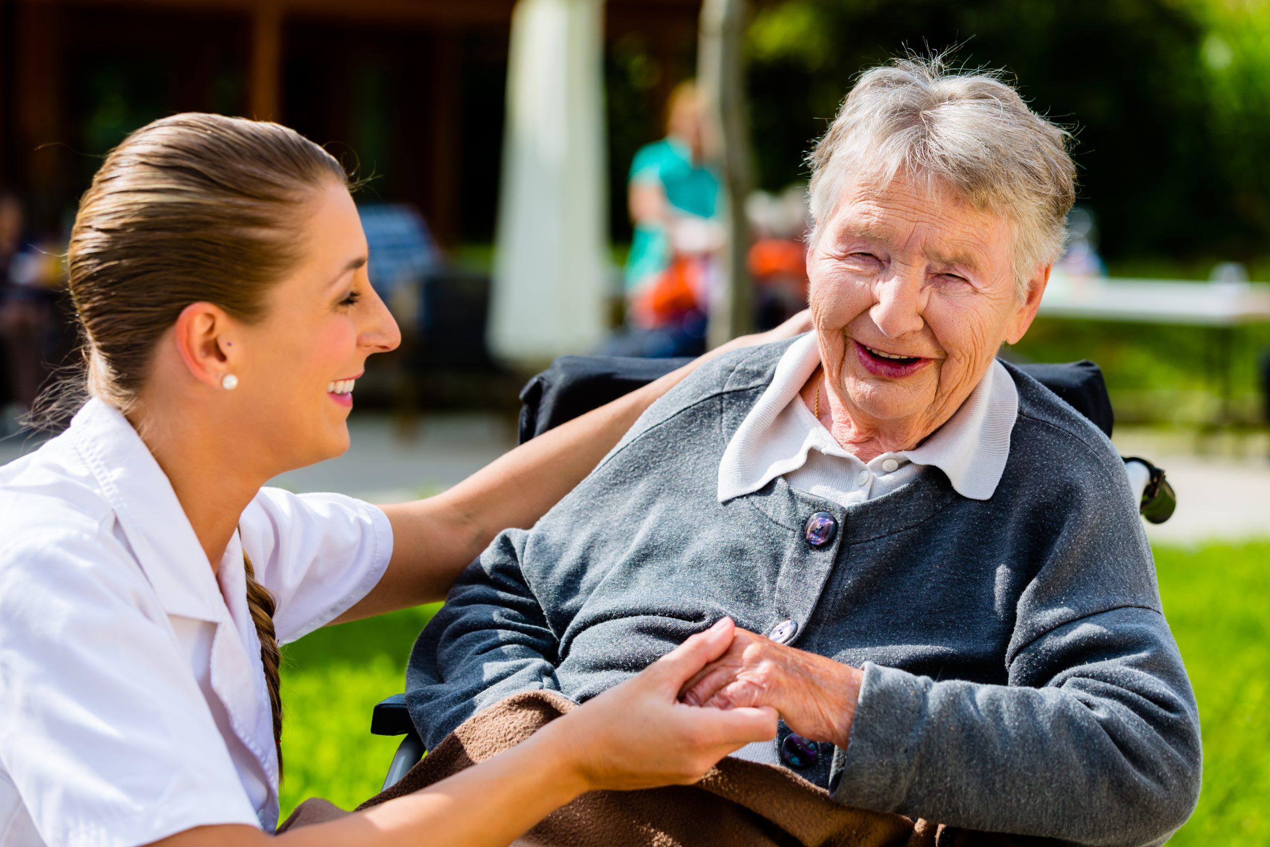 Nurse holding hands with senior woman in wheelchair